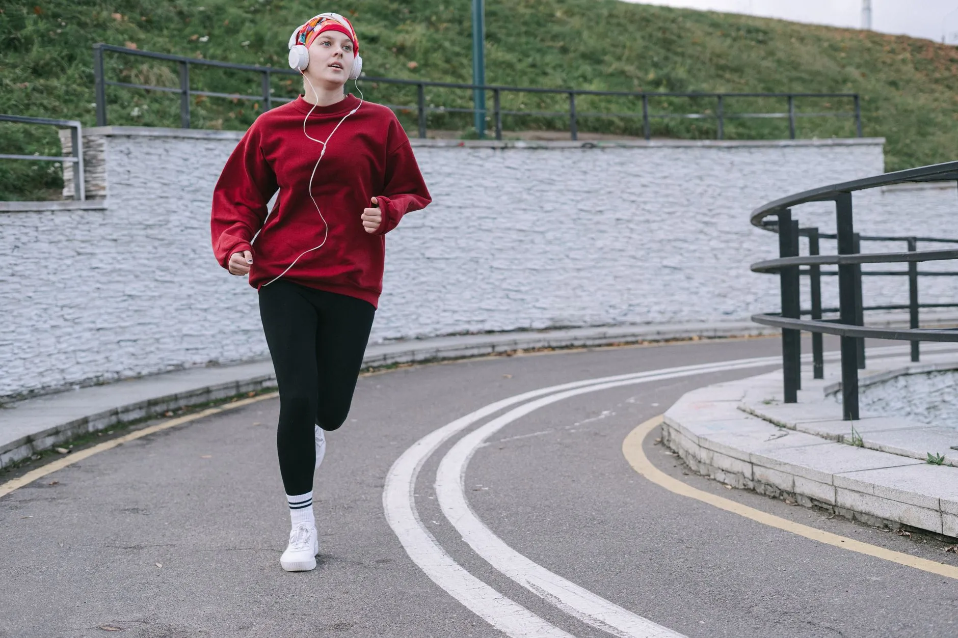 Una mujer con sudadera roja trota por un camino con audífonos puestos, escuchando música.