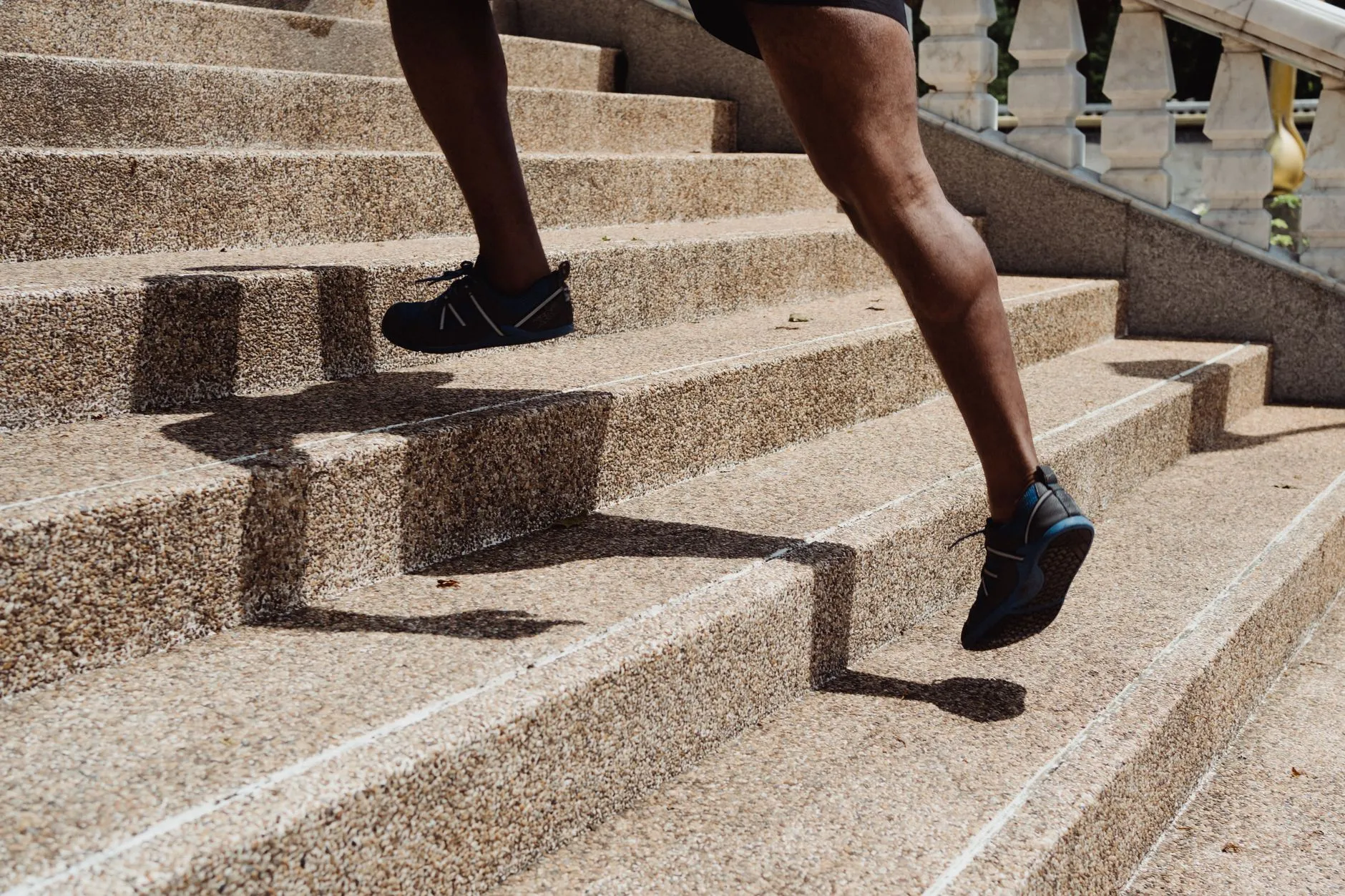 A close crop of someone's legs and sneakers as they climb outdoor concrete stairs quickly in bright sunlight.